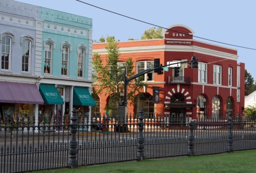 Historic buildings line a street, featuring a colorful shop and a prominent red bank with a decorative facade.