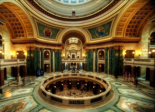 Interior of a grand, ornate building featuring a circular atrium, marble floors, and decorative arches and murals.