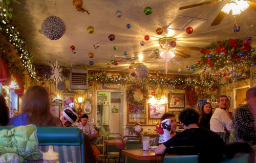 A cozy diner decorated with festive ornaments and lights, filled with people enjoying their meals.