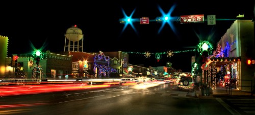 A festive street scene at night, adorned with colorful holiday lights and busy traffic under a starry sky.