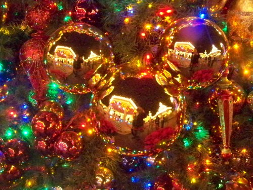 A close-up of colorful Christmas ornaments reflecting festive lights and decorations on a tree.