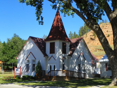A quaint white church with a red steeple, surrounded by trees and a clear blue sky.