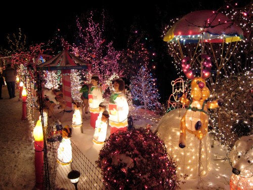 Colorful holiday lights illuminate a snowy scene with festive decorations, including figures and a reindeer.