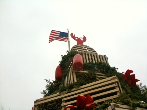A festive structure resembling a Christmas tree, topped with a lobster and an American flag, adorned with red bows.