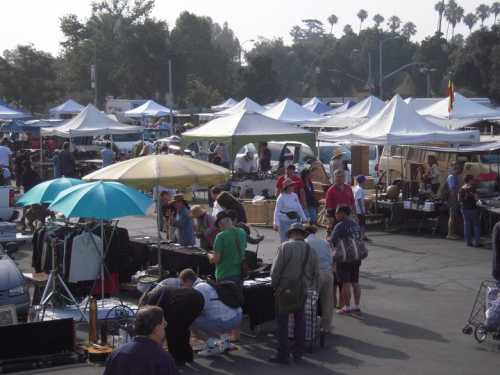 A bustling outdoor market with numerous tents, people browsing items, and colorful umbrellas providing shade.