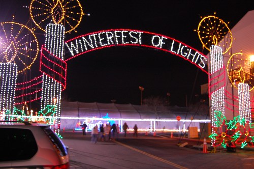 A festive archway reading "Winterfest of Lights" adorned with colorful lights and candles, set against a night sky.