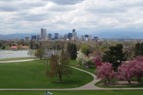 A scenic view of a city skyline with mountains in the background, surrounded by green parks and blooming trees.