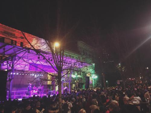 A lively night scene of a crowd at a concert, with colorful stage lights illuminating the performers and audience.