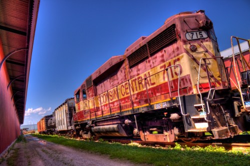 A vintage Wisconsin Central train engine parked beside a building under a clear blue sky.