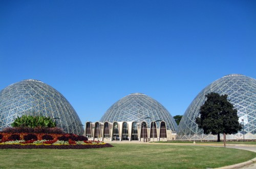 Three large glass domes surrounded by colorful flowers and a clear blue sky.