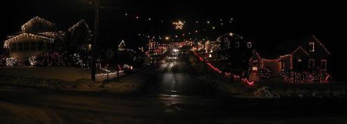 A festive street at night, lined with houses adorned in colorful Christmas lights and decorations.