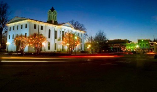 A historic building adorned with festive lights at dusk, with colorful decorations and light trails from passing cars.