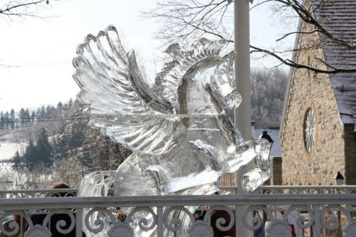 A large, intricately carved ice sculpture of a winged horse stands against a snowy landscape.