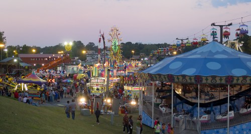 A vibrant carnival scene at dusk, featuring rides, games, and crowds enjoying the festive atmosphere.