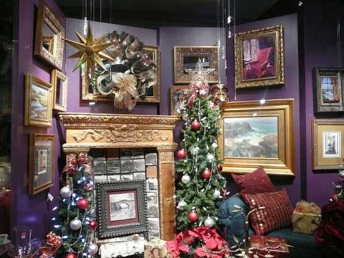 A cozy holiday display featuring a decorated Christmas tree, fireplace, and framed artwork on a purple wall.