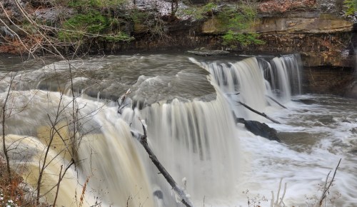 A serene waterfall cascading over rocky ledges, surrounded by lush greenery and a tranquil river.
