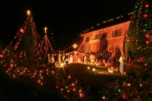A beautifully decorated house with colorful Christmas lights, featuring trees and a nativity scene in the yard.