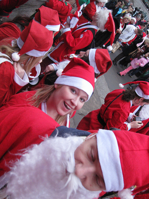 A crowd of people in Santa costumes, some wearing hats and fake beards, celebrating together in a festive atmosphere.