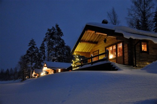 A cozy wooden cabin illuminated at night, surrounded by snow-covered trees and a serene winter landscape.