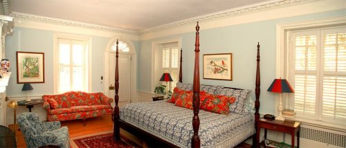 A bright bedroom featuring a four-poster bed, colorful bedding, a floral sofa, and light blue walls.