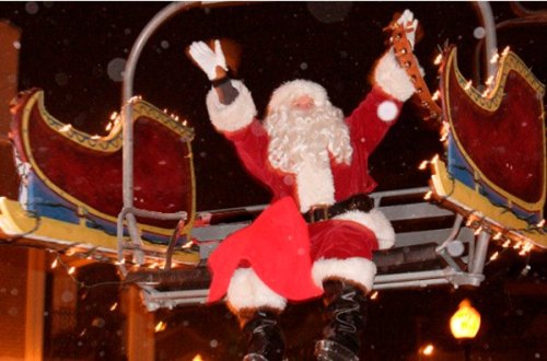 Santa Claus waves from a festive sleigh, surrounded by twinkling lights and falling snow.