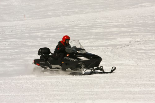 A person in a red helmet rides a black snowmobile across a snowy landscape.