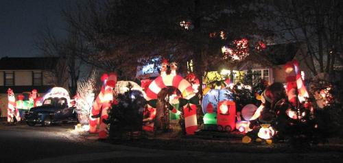 A festive yard display featuring colorful holiday lights, candy canes, and inflatable decorations at night.