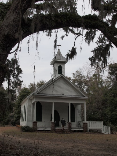 A small white church with a steeple, surrounded by trees and Spanish moss, on a cloudy day.