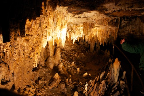 Stalactites and stalagmites illuminated in a cave, showcasing intricate rock formations and textures.