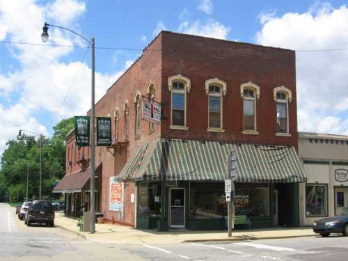 A brick building with large windows and striped awning, located at a street corner under a blue sky with clouds.