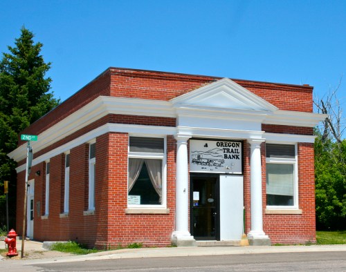 Brick building with white columns and a sign reading "Oregon Trail Bank," set against a clear blue sky.