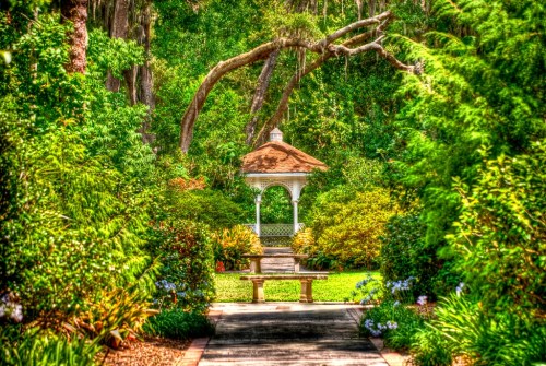 A serene garden path leads to a white gazebo surrounded by lush greenery and colorful flowers.