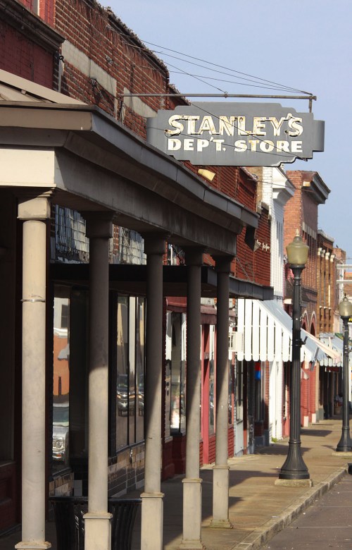 Sign for Stanley's Department Store on a historic street with brick buildings and lampposts.