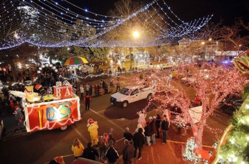 A festive night scene of a parade with colorful lights, decorated floats, and crowds enjoying the celebration.