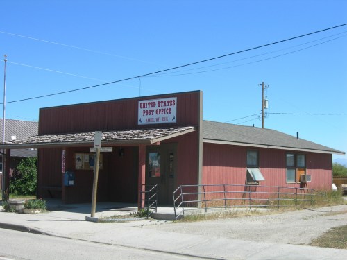 A small, red wooden building with a sign reading "United States Post Office" under a clear blue sky.