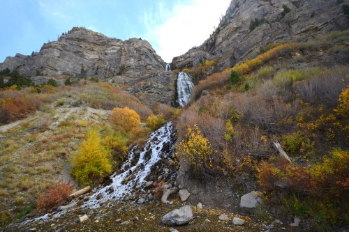 A waterfall cascades down rocky cliffs, surrounded by colorful autumn foliage and rugged terrain.