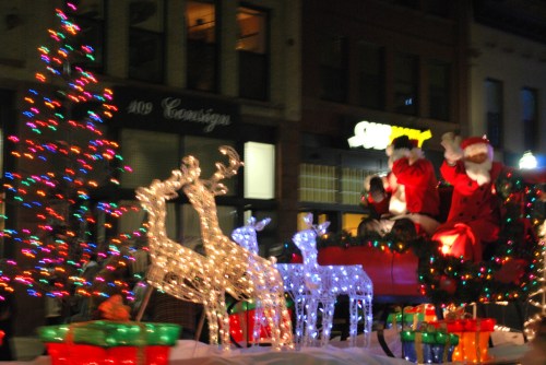 A festive parade scene with illuminated reindeer, Santa Claus, and a decorated Christmas tree.
