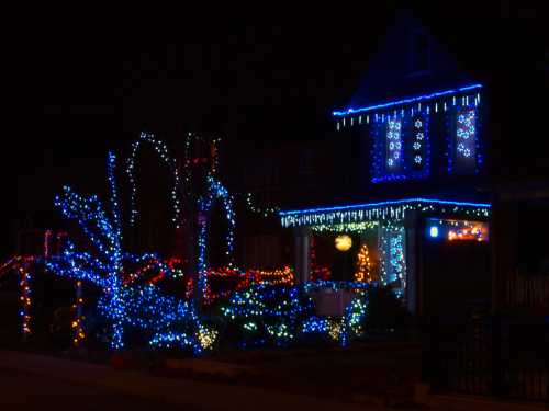 A house decorated with colorful Christmas lights in blue, red, and green, glowing against a dark night sky.