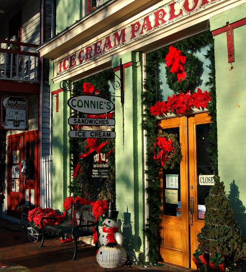 A charming ice cream parlor decorated with festive wreaths and red bows, featuring a welcoming entrance and outdoor seating.