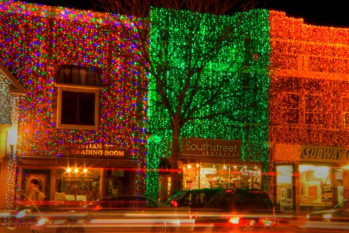 Colorful holiday lights adorn storefronts, with vibrant red and green decorations illuminating the scene at night.