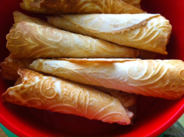 A red bowl filled with intricately patterned, golden-brown rolled pastries.