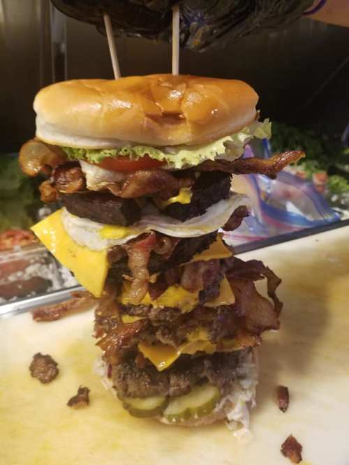 A towering burger stacked with layers of bacon, cheese, lettuce, and patties, held together by toothpicks.