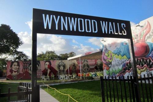 Sign for Wynwood Walls, featuring colorful murals and outdoor seating in a vibrant urban setting.