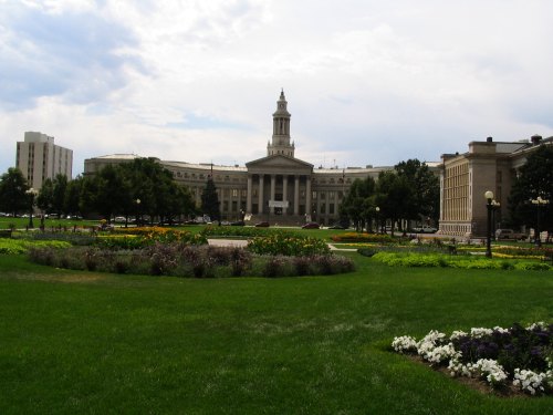 A landscaped park with colorful flowers in the foreground and a historic building with a clock tower in the background.