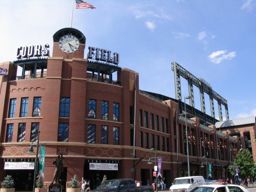 Exterior view of Coors Field, home of the Colorado Rockies, featuring a clock and American flag on a sunny day.