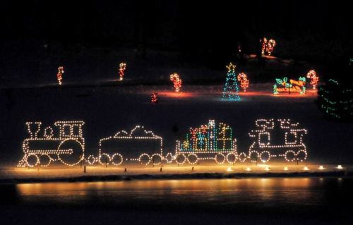 A festive display of a train made of lights, surrounded by colorful holiday decorations in a snowy landscape.