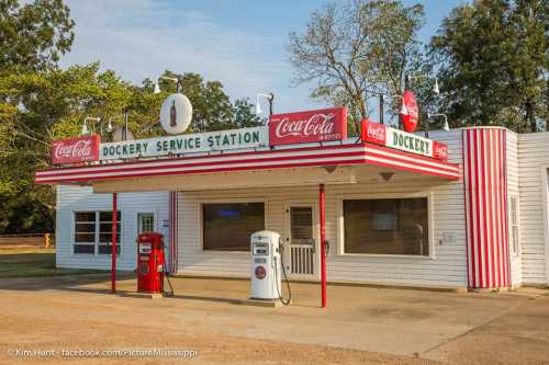 A vintage service station with red and white stripes, featuring Coca-Cola signage and classic gas pumps.