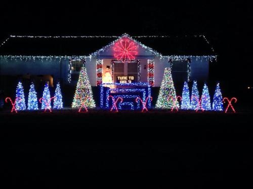 A house decorated with colorful Christmas lights, featuring trees, candy canes, and a large snowflake display.