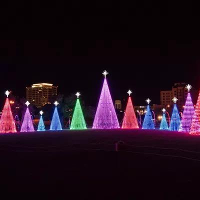Colorful illuminated Christmas trees in a park at night, featuring vibrant lights and star toppers.