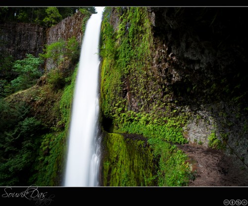 A cascading waterfall surrounded by lush green vegetation and rocky cliffs, creating a serene natural scene.